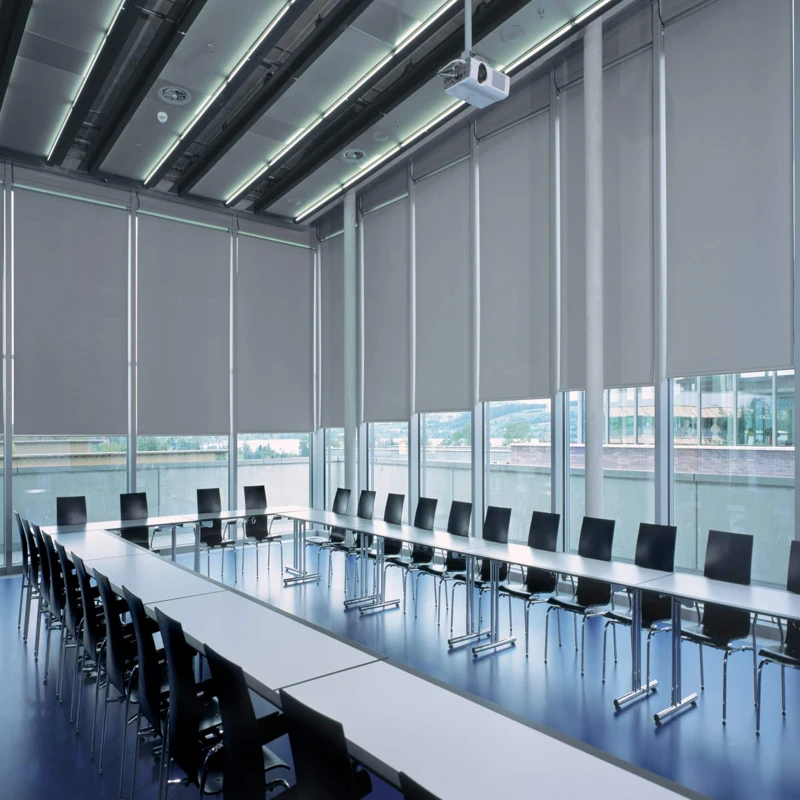 motorized gray roller blinds partially lowered over large windows in a modern office